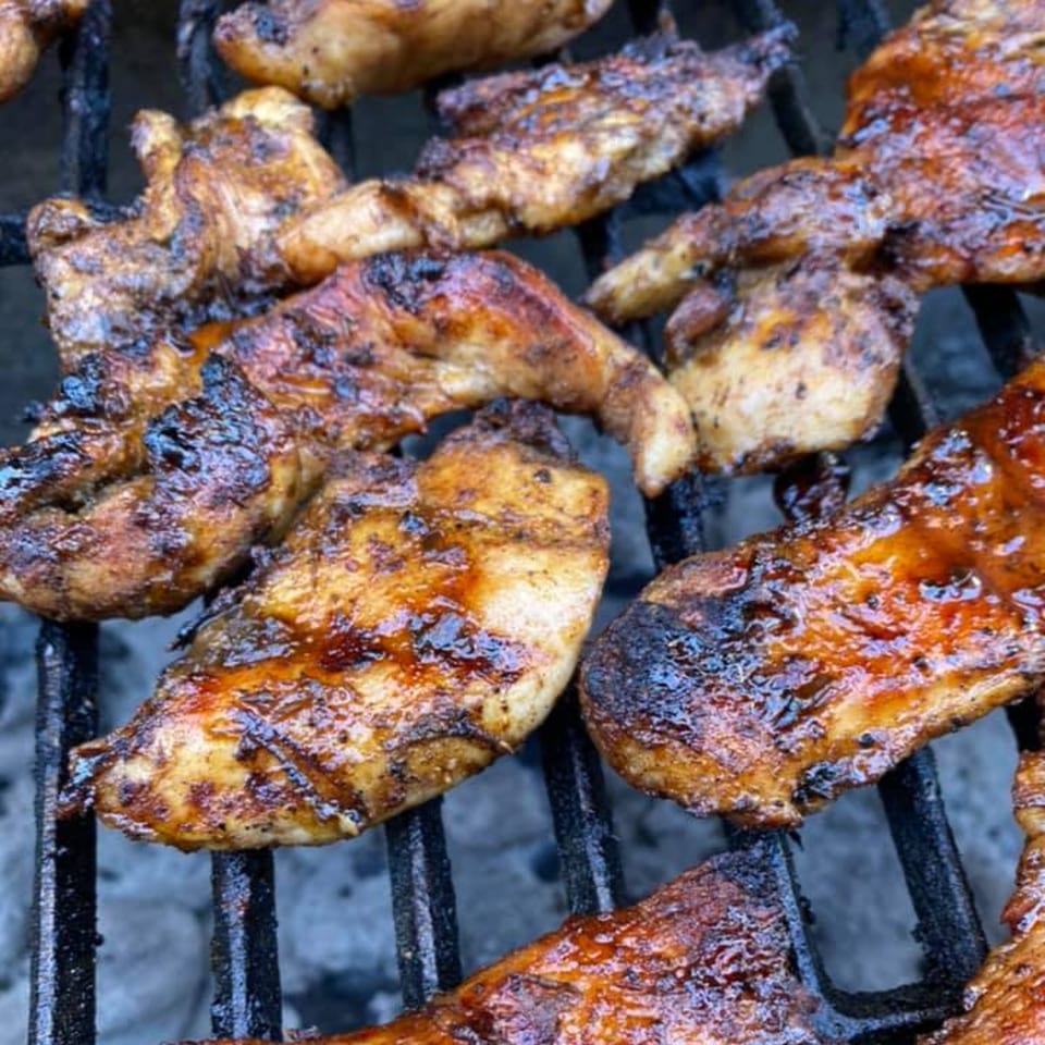 Close-up of Rasta Kitchen's jerk chicken pieces grilling on a dark metal grate.