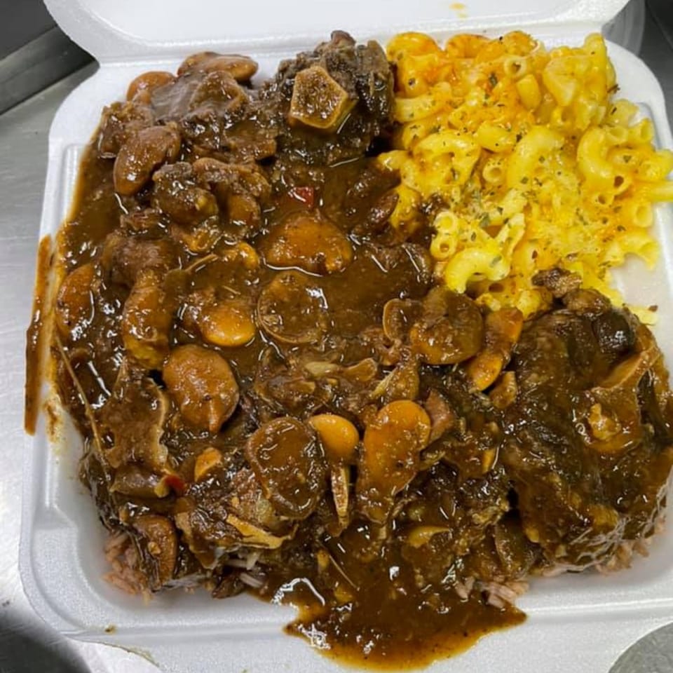 A takeout container filled with Jamaican oxtail stew, rice, and a side of macaroni and cheese.