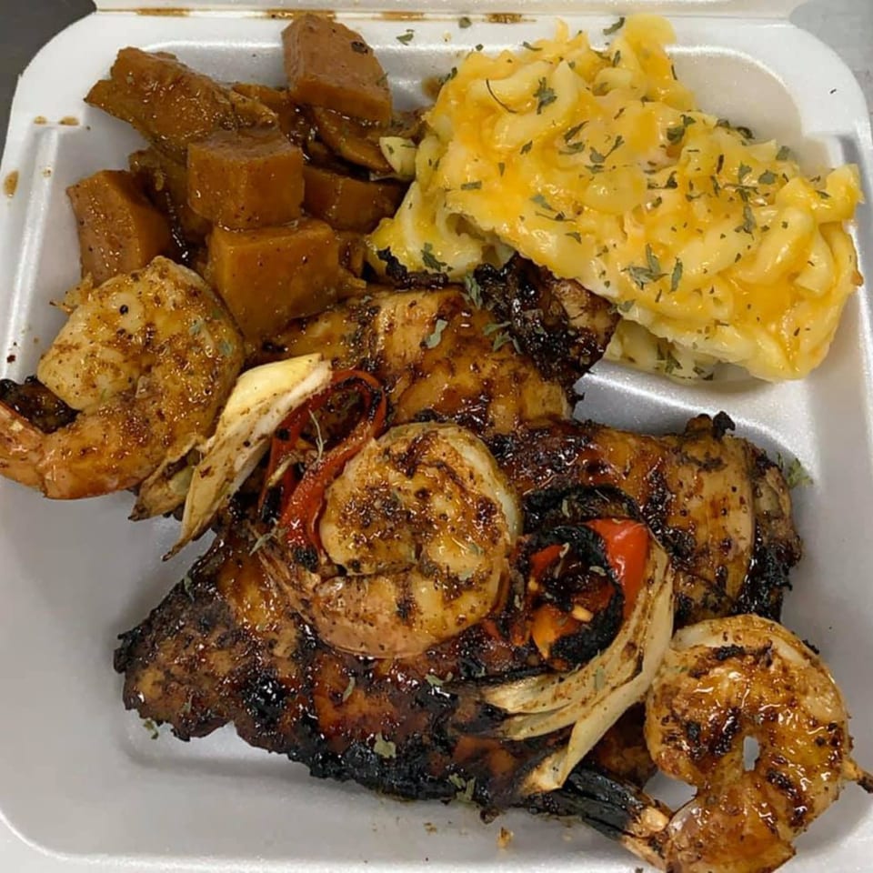 Rasta Kitchen's jerk chicken and shrimp with mac and cheese and sweet potatoes in a takeout container.